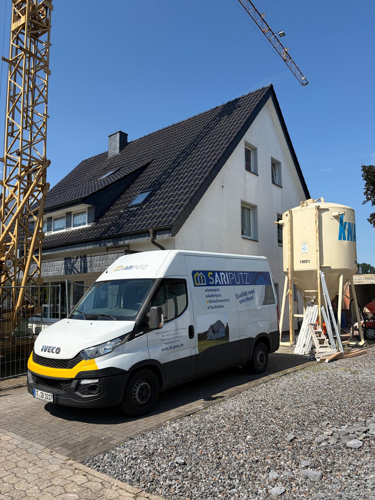 Dreifamilienhaus mit Satteldach während der Kernsanierung, davor ein SARI PUTZ-Transporter, ein Knauf-Putzsilo und ein Baukran